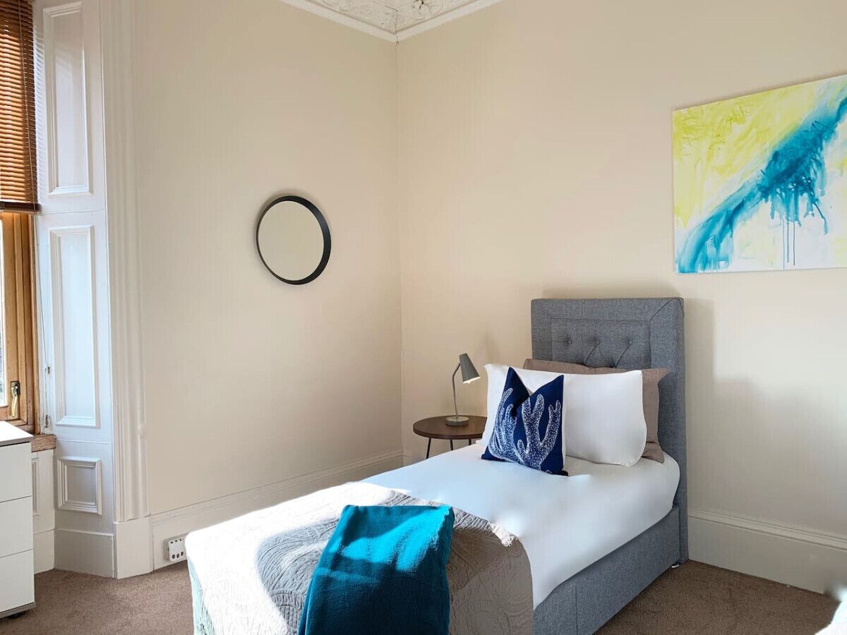 A bedroom with a bed, a bedside table, a lamp, a wall clock, and a painting.