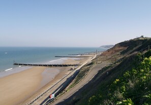 A coastal beach with a wooden walkway, a pier, and a distant hill.