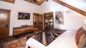 Une chambre spacieuse avec un grand lit, des poutres apparentes en bois au plafond, un ventilateur de plafond et une table de chevet avec des verres à vin.