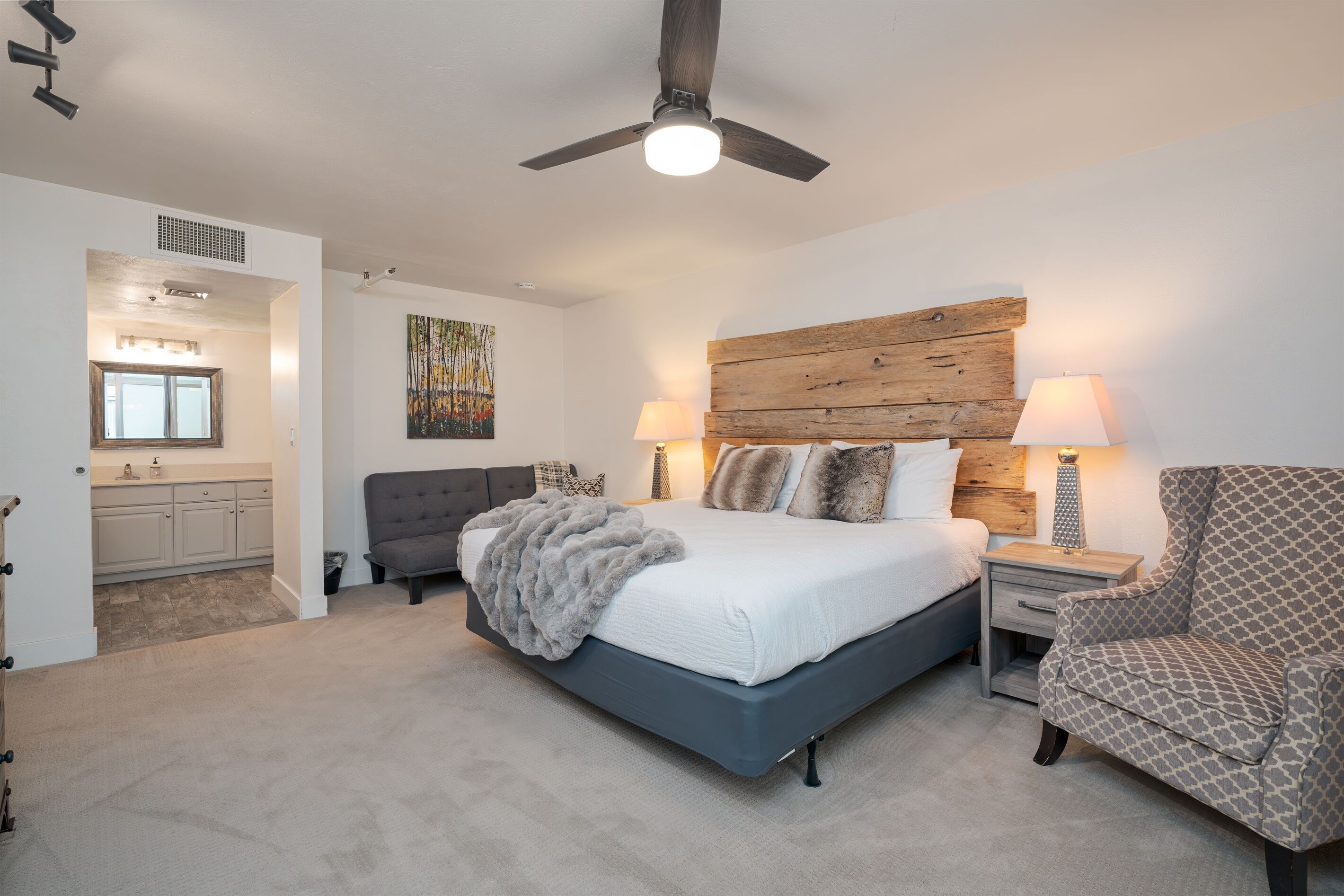 A bedroom with a large bed, a wooden headboard, two bedside lamps, a chair, and a ceiling fan.