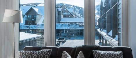 A room with a view of a snowy landscape through large windows, a sofa with patterned cushions, and a floor lamp.