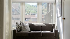 A dark brown sofa with patterned cushions in a room with large windows overlooking a hilly landscape. - Ski in Ski out with a view. Fantastic 2 bed condo. (Park City)