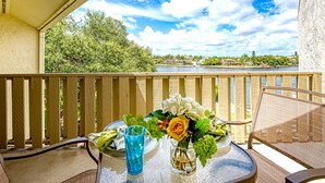 A balcony with a table set for two, overlooking a river with a view of houses and greenery. - Luxury Waterfront Views / Pool / 1400sf / Minutes to Beach (Siesta Key)