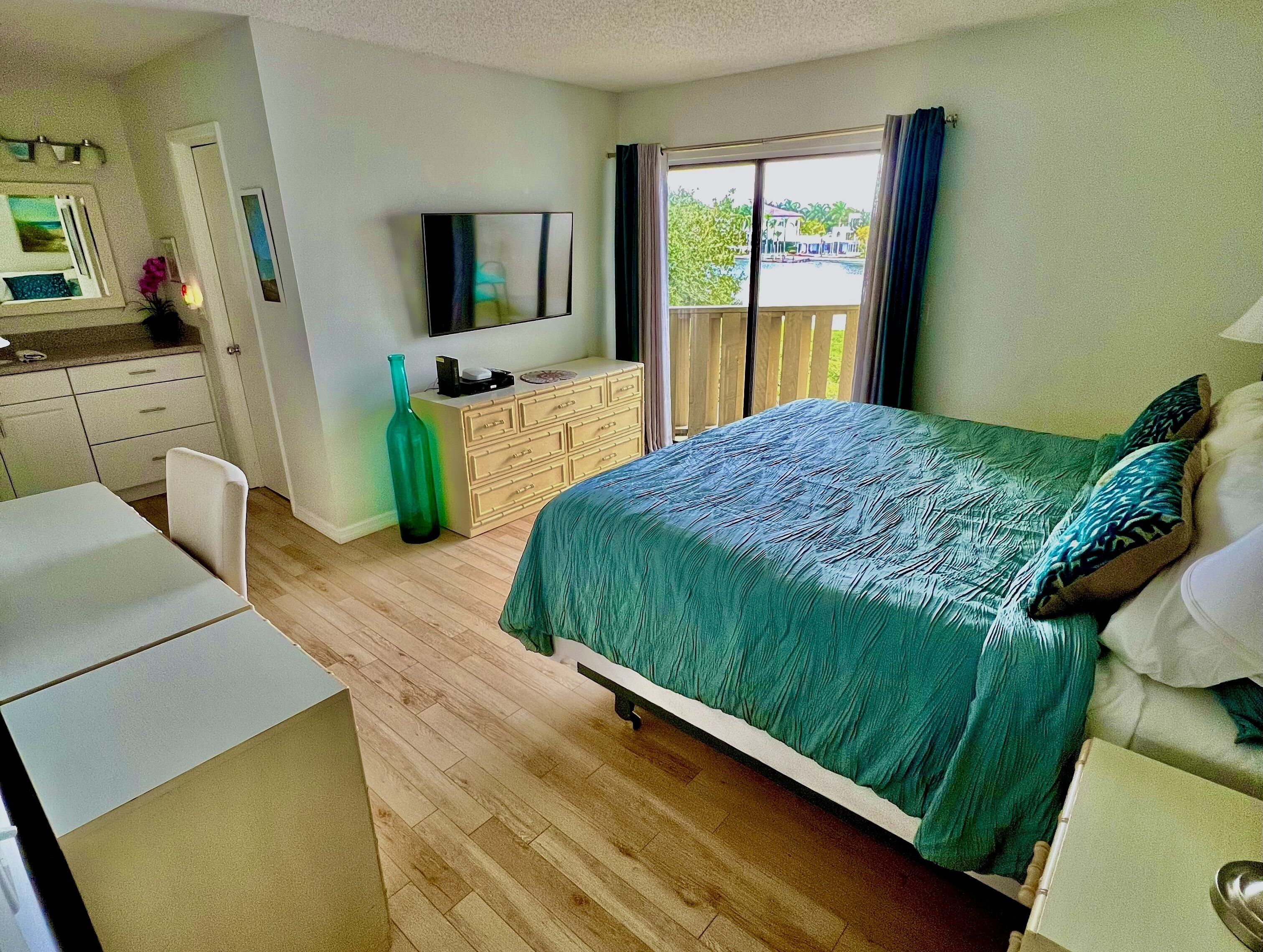 A bedroom with a bed, a dresser, a television, and a window with curtains.