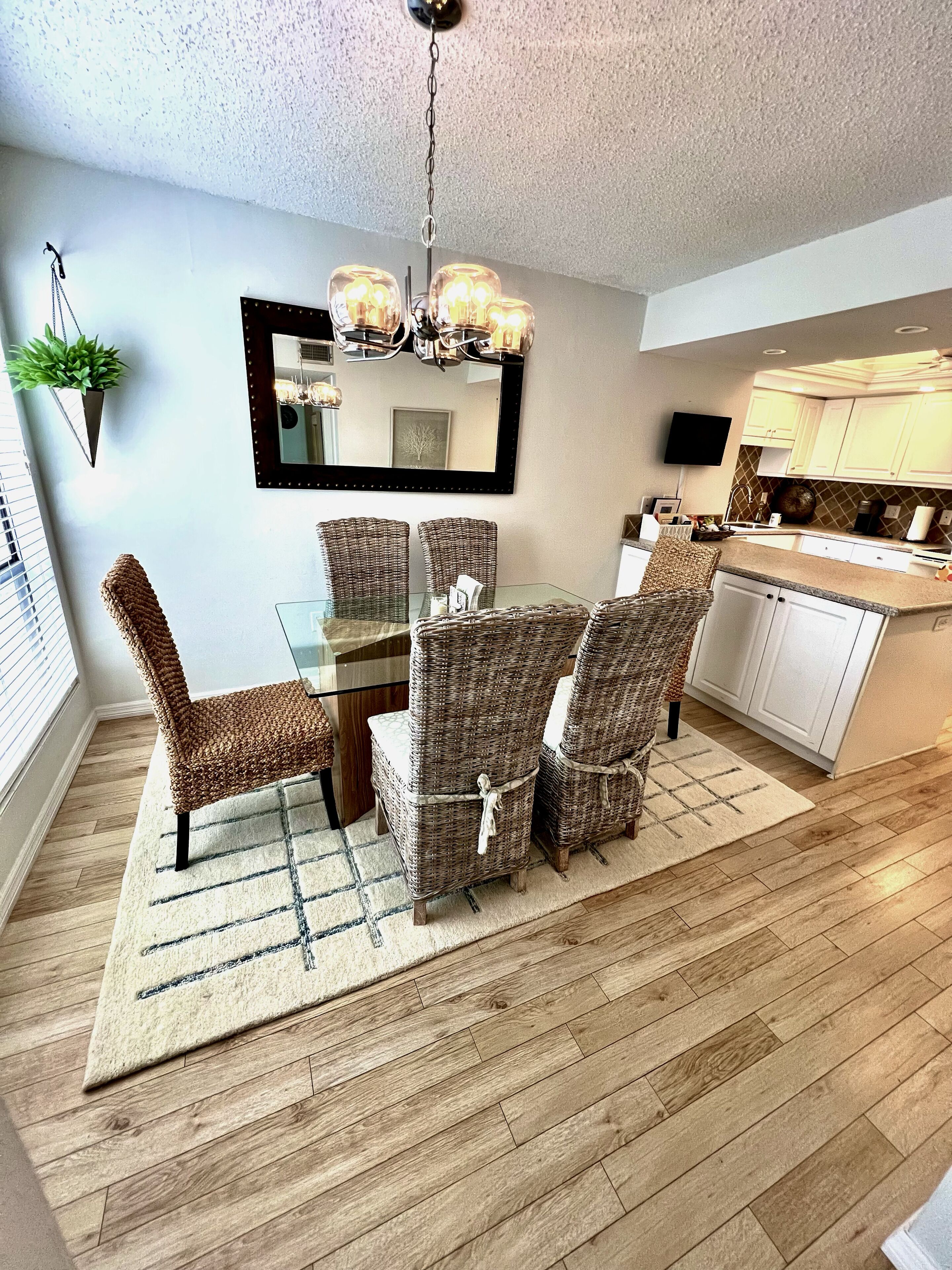 A dining area with wicker chairs, a glass table, and a chandelier.