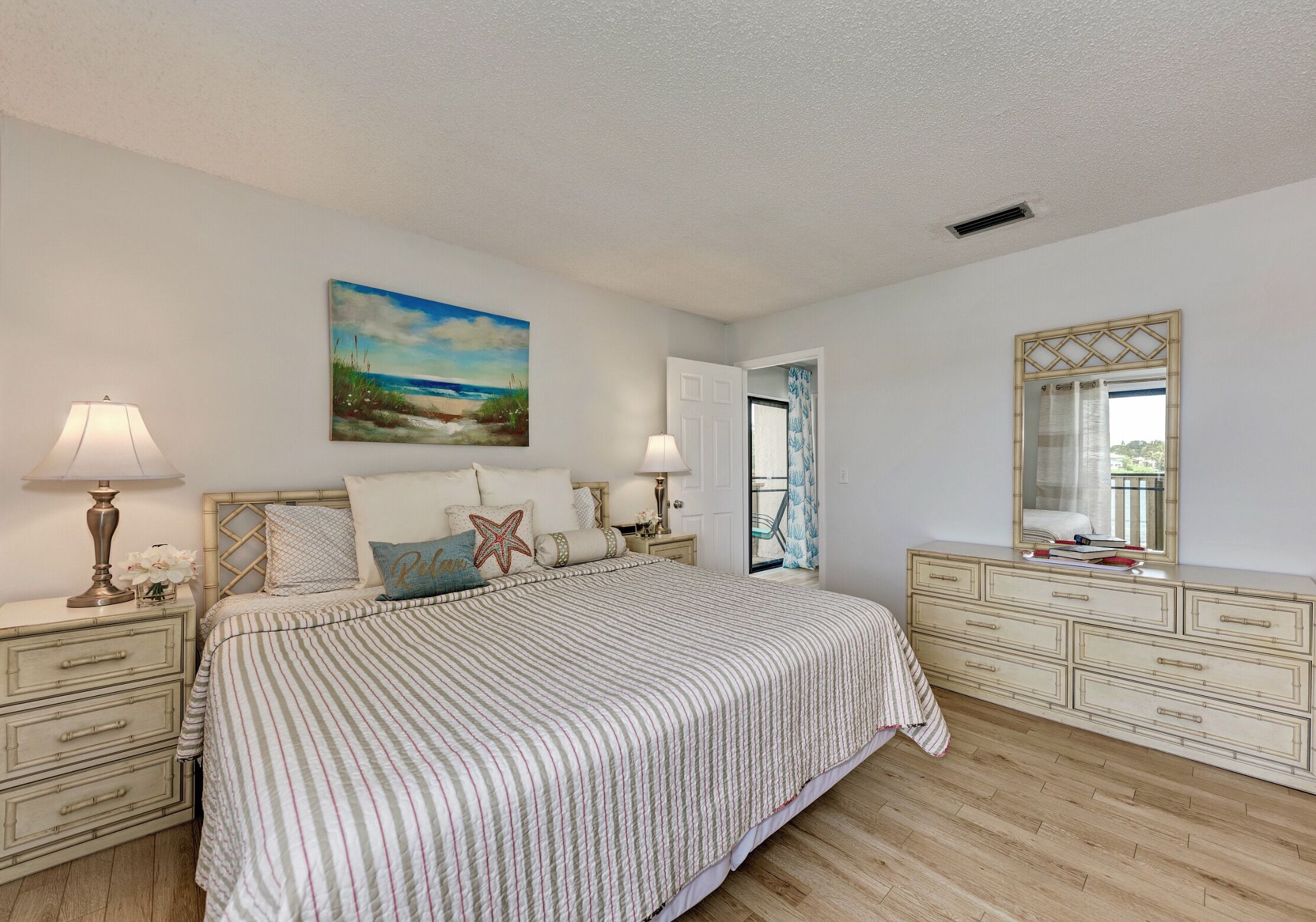 A bedroom with a large bed, bedside tables, a dresser, a painting, and a mirror.