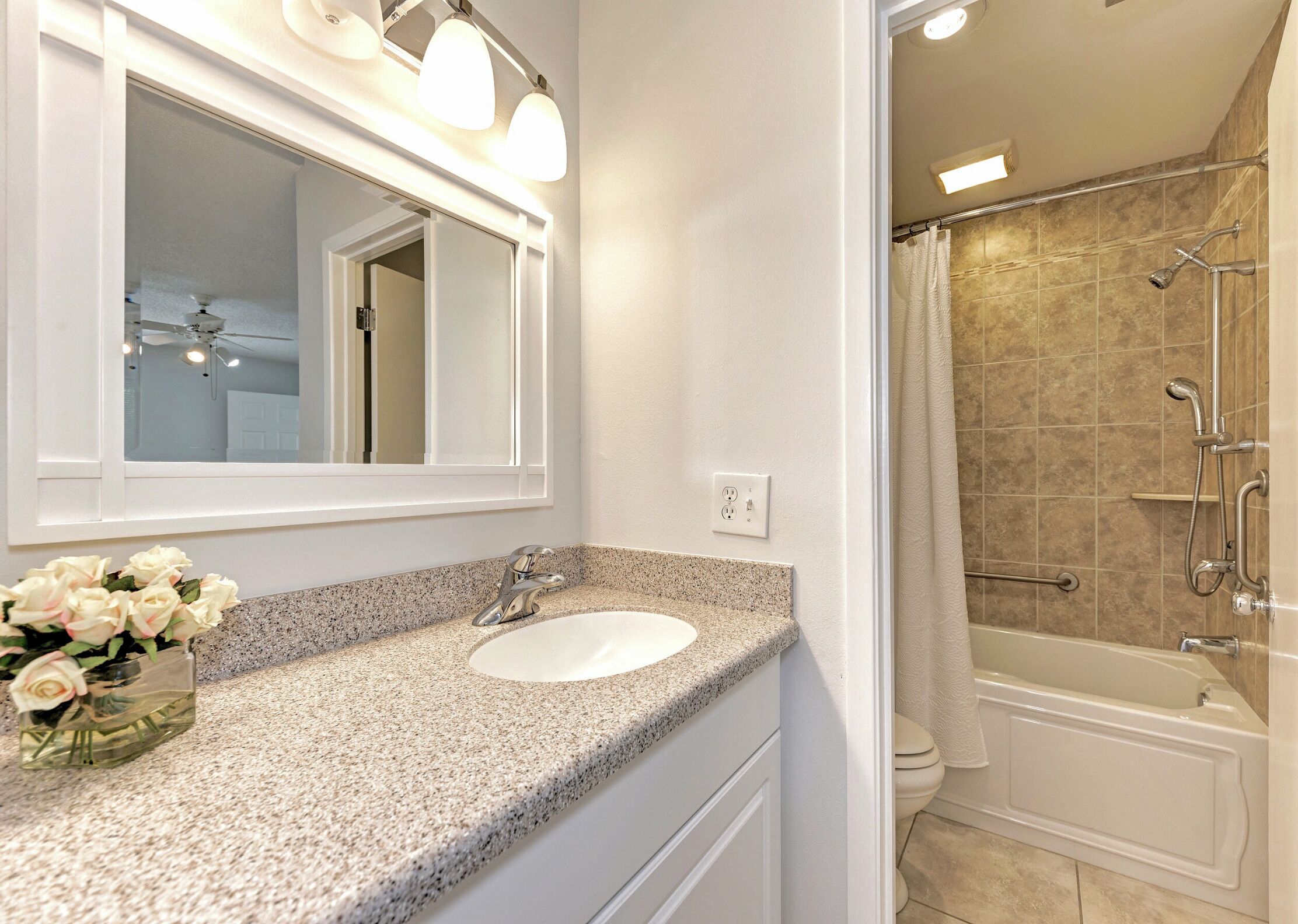 A bathroom with a granite countertop, a white sink, a mirror, and a shower area.