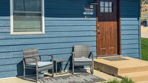A blue house with a wooden door, two wicker chairs, a small table, and a welcome sign.