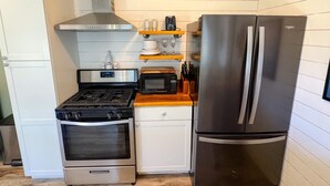 A compact kitchen with a gas stove, oven, microwave, and a stainless steel refrigerator.
