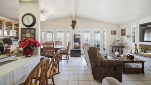 A spacious living area with a dining table, chairs, a sofa, and a kitchen area with cabinets and a clock.