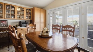 A dining area with a wooden table and chairs, a kitchen with wooden cabinets, and a view through large glass doors.