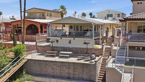 A residential area with a two-story house featuring a balcony, a patio with outdoor furniture, and a staircase leading to an upper level.