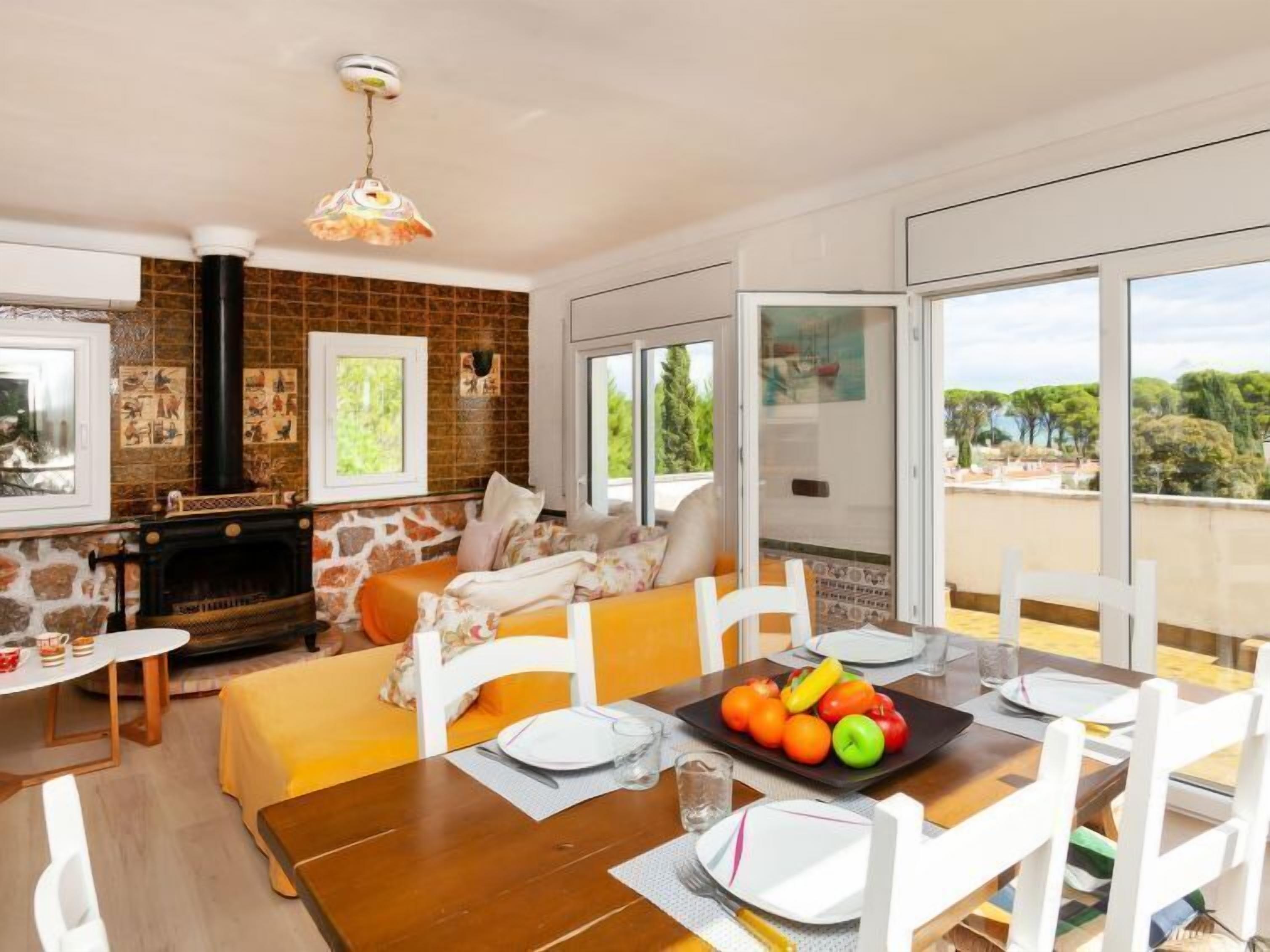 A modern living room with a fireplace, a dining area with a table set for two, and large windows offering a view of the outdoors.