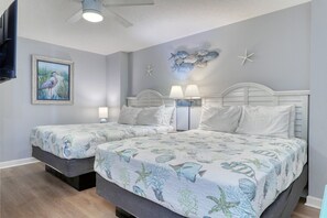 A bedroom with two beds, each with a white headboard and matching bedding. There is a ceiling fan, a wall-mounted TV, and a framed picture of a bird. - HS-1127 Ocean View Condo in Myrtle Beach - 1 Bedroom, Sleeps 6 (Myrtle Beach)