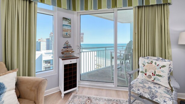 Un balcón con vista al mar, una silla con un cojín decorativo y una pequeña mesa con un adorno.