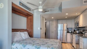 Un dormitorio con cama, ventilador de techo, kitchenette con refrigerador y baño con inodoro.
