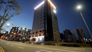 A high-rise building with illuminated windows and a well-lit entrance, surrounded by other tall buildings. - Hound Hotel Gijang (Busan)