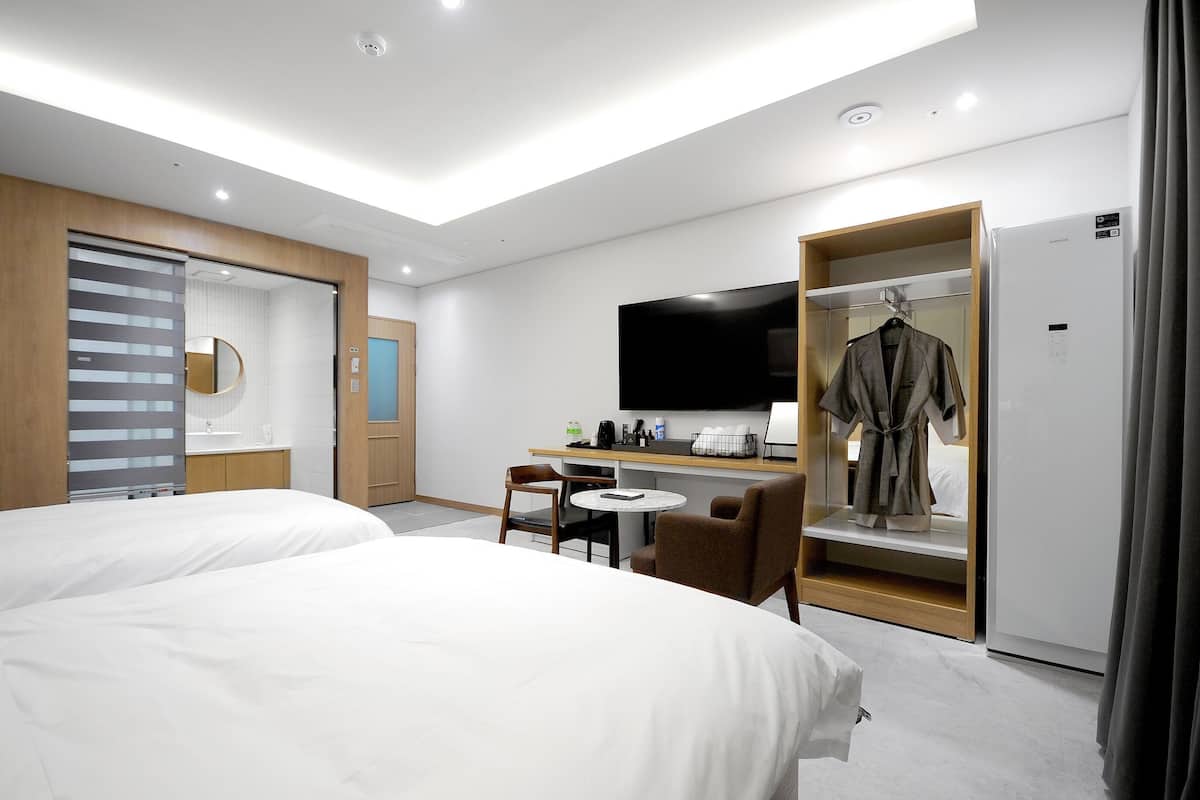 A hotel room with two beds, a desk with a chair, a television, and a wardrobe.