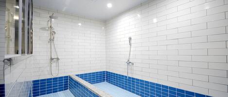 A modern bathroom with white and blue tiles, a shower area, and a glass-enclosed window.