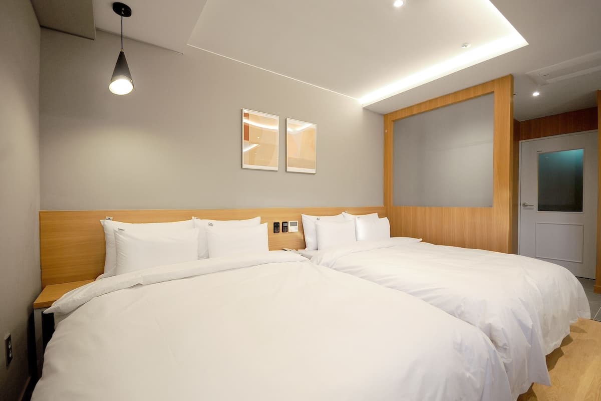 A hotel room with two beds, a wooden headboard, a ceiling light, and a door with frosted glass.