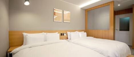 Habitación de hotel con dos camas, cabecero de madera, lámpara de techo y puerta con vidrio esmerilado.