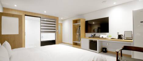 A hotel room with a large bed, a desk with a chair, a TV, and a wardrobe.