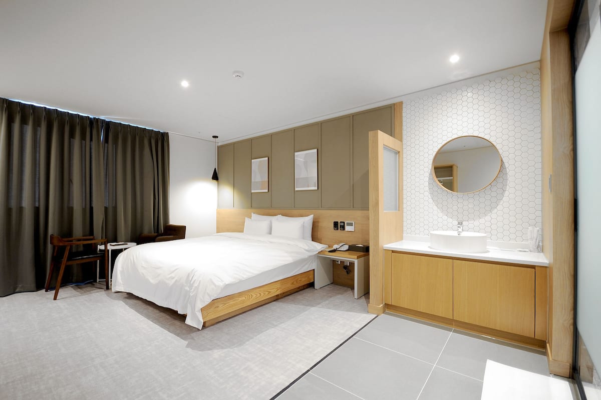 A modern hotel room with a large bed, bedside table, and a bathroom with a sink and mirror.