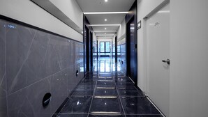 A modern hotel corridor with marble walls, a black-tiled floor, and recessed lighting. - Hound Hotel Gijang (Busan)