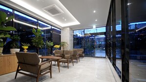A modern indoor seating area with a glass wall, large potted plants, and a clean, tiled floor. - Hound Hotel Gijang (Busan)