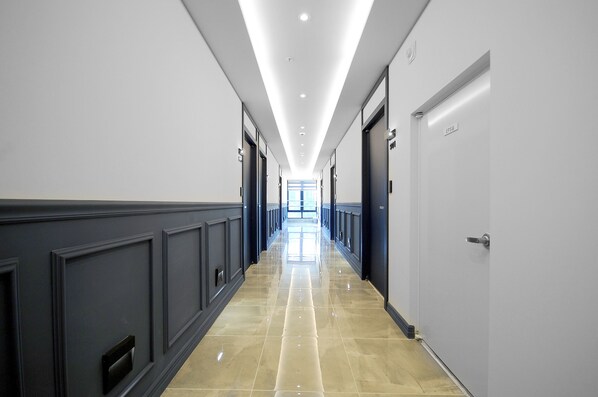 A long, narrow hallway with a shiny, reflective floor and a series of doors on both sides.