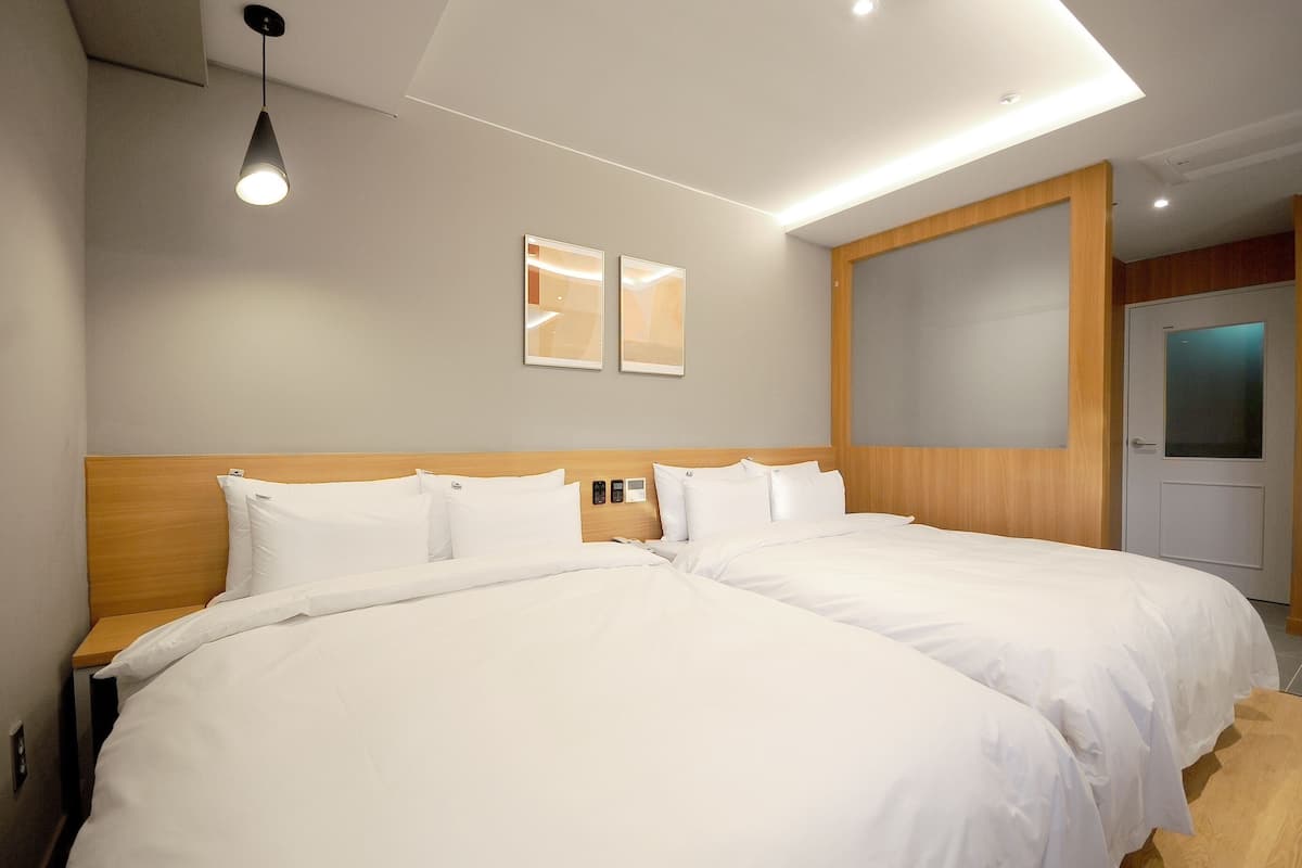 A hotel room with two beds, a wooden headboard, a ceiling light, and two framed pictures on the wall.