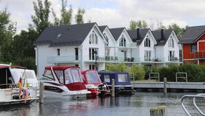 Reihenweise weiße Häuser mit dunklen Dächern und Balkonen, angestoßene Boote und ein ruhiges Gewässer.