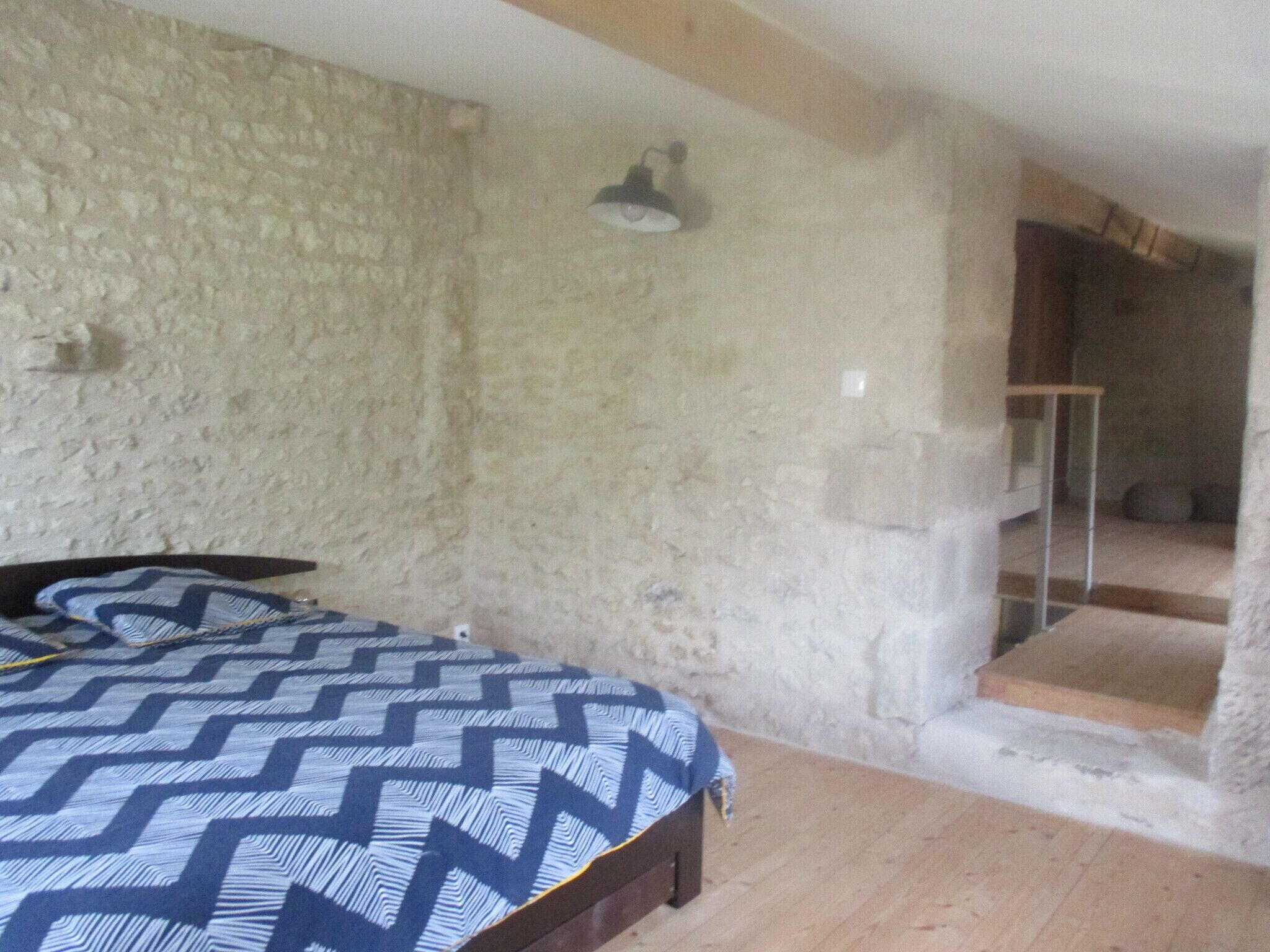 Un dormitorio con cama, pared de piedra, escalera y una mesita.