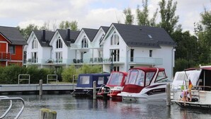 A row of modern houses with balconies, a dock with boats, and a calm water body.