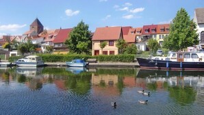 A calm river with boats and ducks, surrounded by houses with red roofs and a church tower.