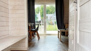 A room with a wooden floor, a dining table with chairs, a bench, and a sliding glass door leading to a garden. - Apartment in Dziwnów by Baltic Sea Beach (Dziwnow)