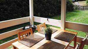 A wooden table with four chairs and woven placemats, set on a deck with a view of a green lawn and a wooden fence.