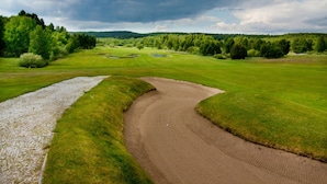 A golf course with a gravel path, green grass, and trees under a cloudy sky.