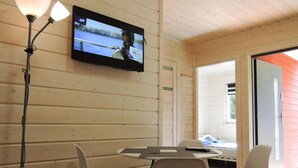 A room with a TV mounted on the wall, a table with chairs, and a bed with a window.