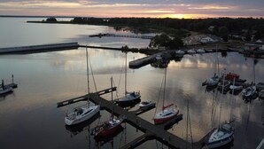 A marina with multiple boats docked at piers, surrounded by calm water and a sunset in the background.