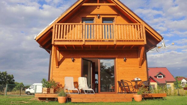 A wooden cabin with a balcony, a sliding glass door, and outdoor seating.