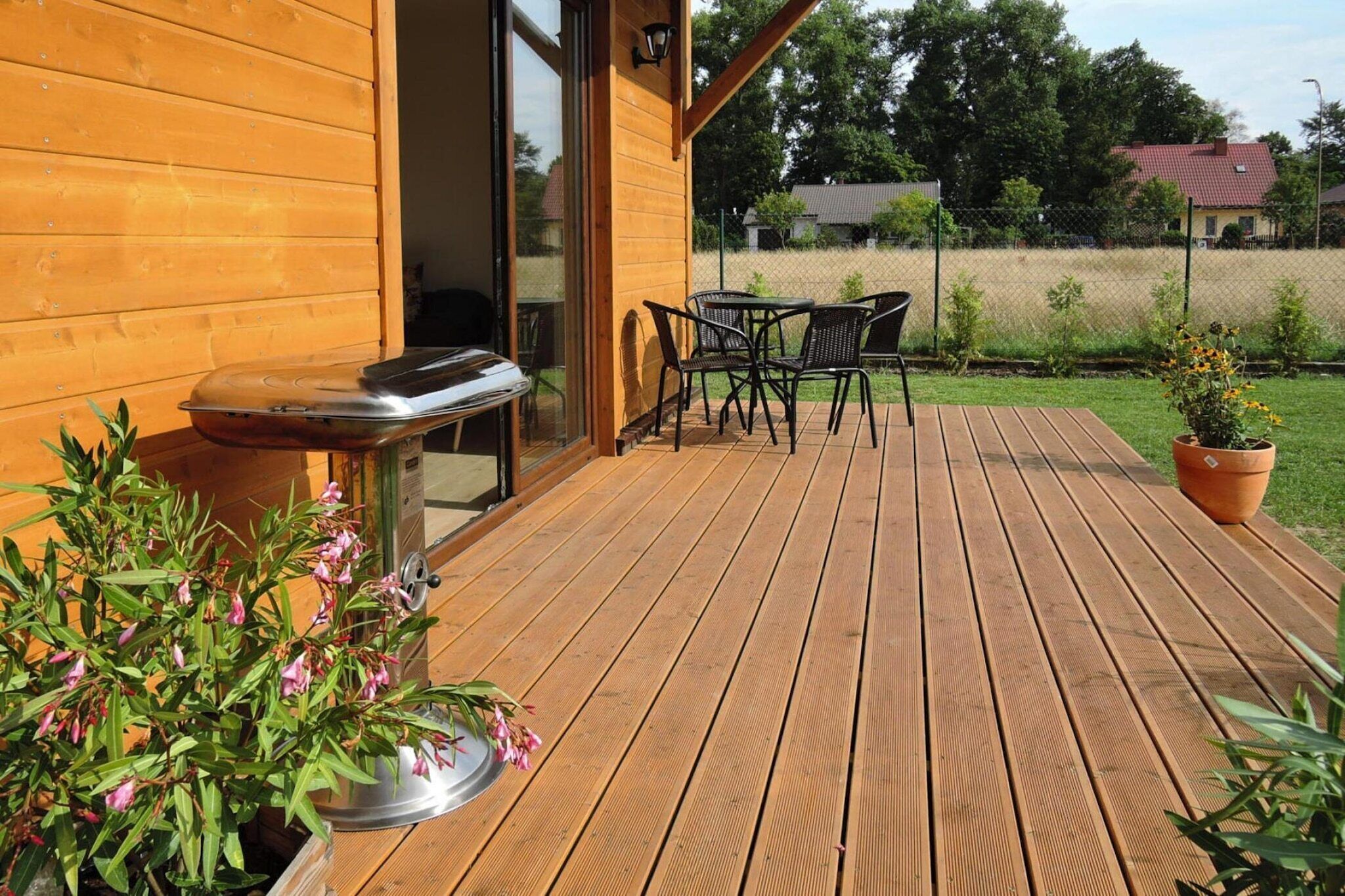 Une terrasse en bois avec un barbecue, des chaises et un pot de fleurs.