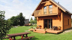 A wooden cabin with a balcony, a patio with seating, and a picnic table in the yard.