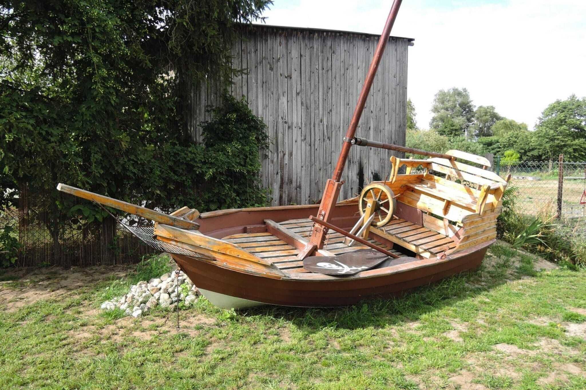 A small wooden boat with a rudder and oar, docked near a wooden shed in a grassy area.