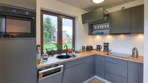 A modern kitchen with grey cabinets, a built-in oven, a dishwasher, and a window overlooking a garden.