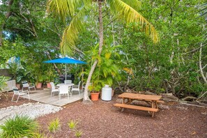 An outdoor patio with a wooden table and chairs, a blue umbrella, and a barbecue grill. - Key West Oasis! 2BR Villa with Pools and Marina at Coconut Mallory Resort (Key West)