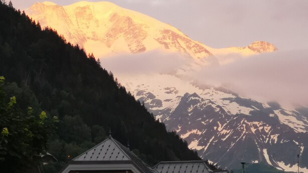 A building with a sign reading "MAISON DE SAINT-GERVAIS" and "OFFICE DE TOURISME," surrounded by mountains and trees.