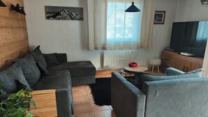 A living room with a sectional sofa, a round coffee table, a television, and a radiator.