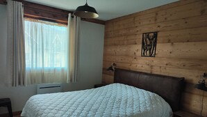 A bedroom with a bed, a window with curtains, a wooden wall, and a ceiling light.