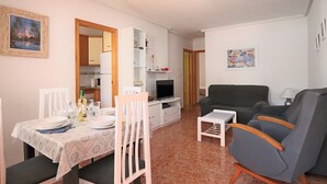 A living room with a sofa, TV, and a dining area with a table set for two. - 001 - Altomar II 001 - comfortHOLIDAYS (Santa Pola)